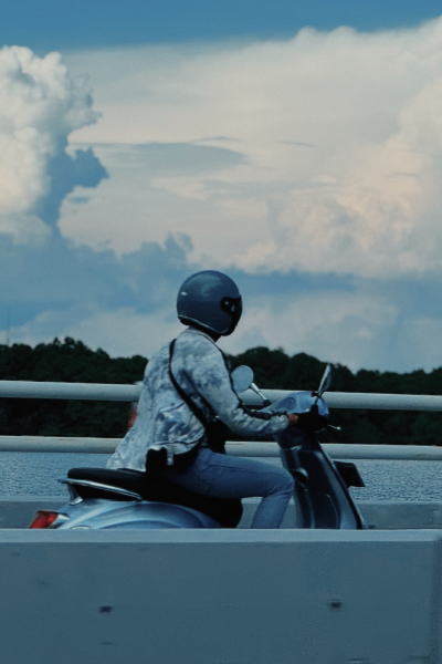 Person in helmet riding a scooter on a bridge with dramatic clouds in the sky