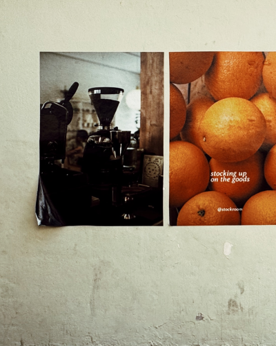 Posters on a wall, one showing a coffee grinder, the other oranges with text
